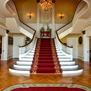 Grand staircase with red carpet in a luxurious hotel lobby, highlighted by a chandelier.
