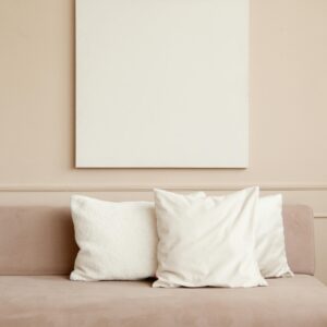 A minimalist living room with a beige sofa and a blank canvas on a neutral wall.